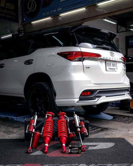 รถสีขาว มีโช๊คอัพสีแดงวางอยู่ตรงพื้นข้างๆ 