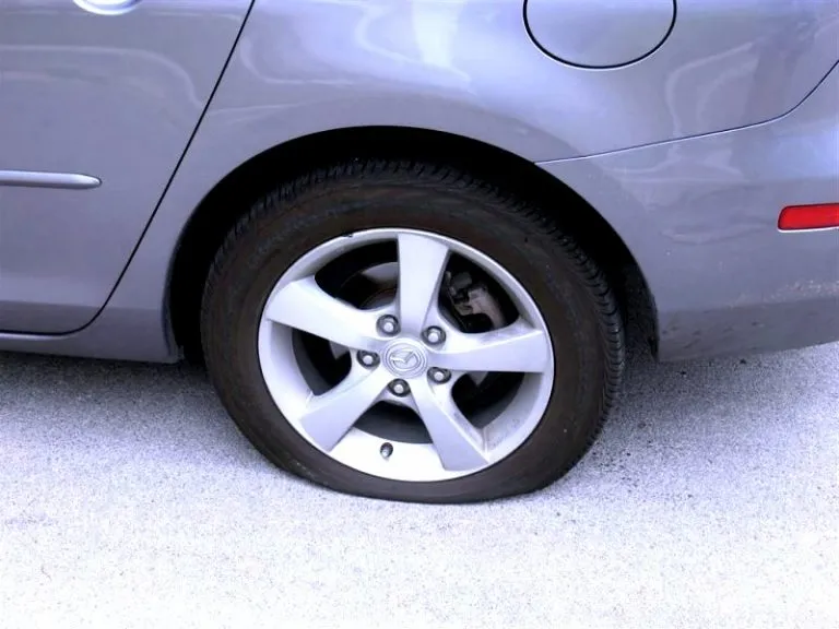 รถเก๋งยี่ห้อ Mazda สีเทายางแบน จอดอยู่บนพื้นคอนกรีต