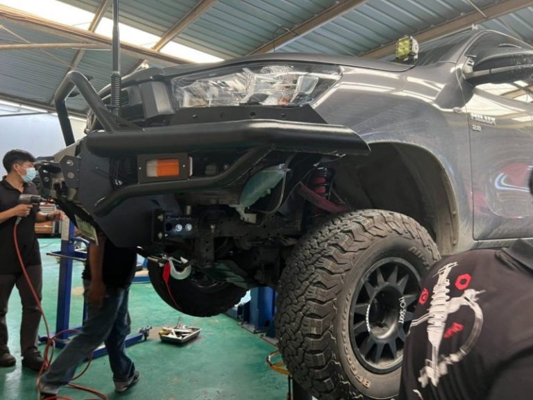 พนักงานกำลังติดตั้งซ่อมช่วงล่างรถกระบะออฟโรดคันสีดำ ที่ถูกยกสูงในอู่รถ