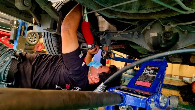 ช่างผู้ชายสวมแมสตรวจเช็คช่วงล่าง โดยมือกำลังถือโช๊คอัพ